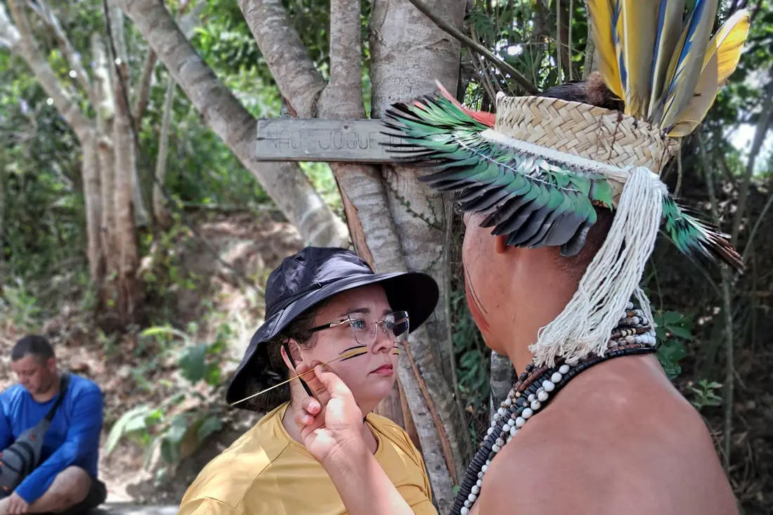 Indígena Pataxó fazendo pintura tradicional no rosto de uma visitante